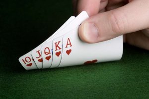 Ilustracija kombinacije rojal fleša u pokeru: karte A–K–Q–J–10 iste boje poređane na zelenom stolu sa poker žetonima.